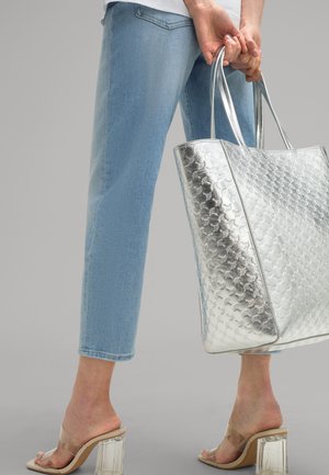 Zilveren draagtas met een gestructureerde afwerking, gecombineerd met lichtblauwe cropped jeans en transparante blokhak sandalen. Eenvoudig, modern ontwerp.