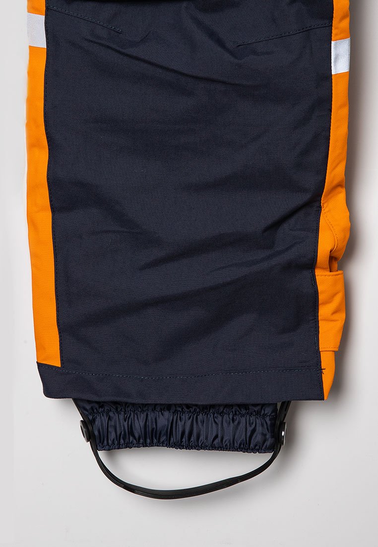 Marina- och orangefärgade vattentäta byxor med elastisk stånd och dragsko. Reflekterande remsa längs sidan. Hållbart tyg med en slät textur.