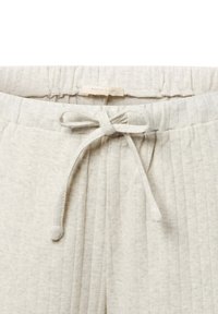 Lichtbeige ribbel loungebroek met een elastische tailleband, trekkoordsluiting en subtiel textuurpatroon. Merkenlabel zichtbaar.