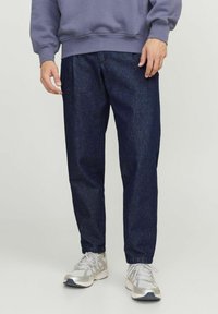 Donkerblauwe spijkerbroek met een losse fit, gecombineerd met een grijze sweatshirt en zilveren sneakers. Effen stof zonder zichtbare patronen of accenten.