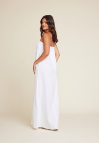 Hvit langermet maxikjole uten stropper laget av lett stoff, med løs passform, glatt tekstur og ankellang design. Ingen synlige mønstre eller detaljer.