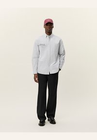 Chemise à rayures légère bleu et blanche, associée à un pantalon noir et une casquette bordeaux avec le texte "Lower West Side". Tissu lisse.