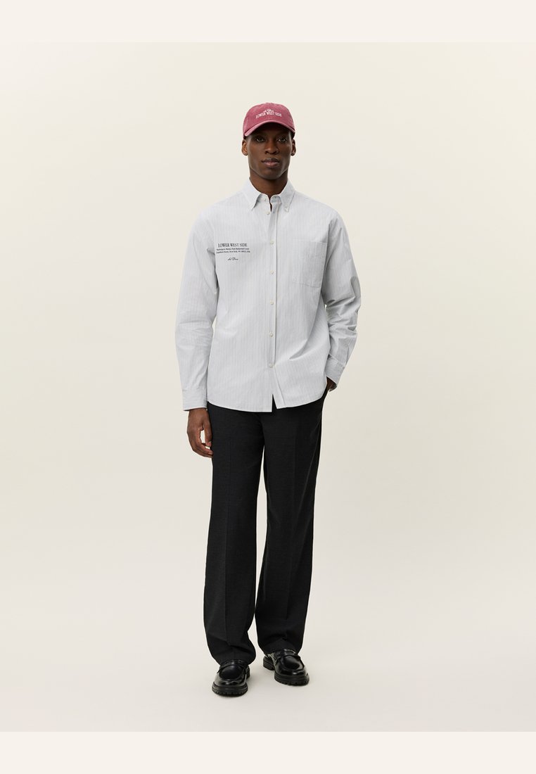 Chemise à rayures légère bleu et blanche, associée à un pantalon noir et une casquette bordeaux avec le texte "Lower West Side". Tissu lisse.