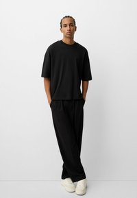 Tricou oversize negru cu mâneci scurte, asortat cu pantaloni negri, largi și adidași albi. Design simplu, minimalistic.