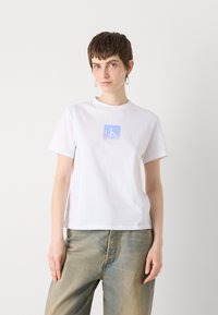 Tricou alb din bumbac, cu un mic logo "ck" în degradeu albastru pe piept, guler clasic și mâneci scurte.