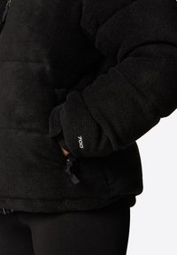 Czarna polarowa kurtka z wysokim kołnierzem, długimi rękawami i prążkowanymi mankietami. Posiada regulowany sznurek ściągający u dołu oraz detal "700" na rękawie.