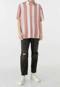 Camicetta a maniche corte con bottoni, a righe verticali rosa e bianche; abbinata a jeans neri strappati e sneakers bianche.