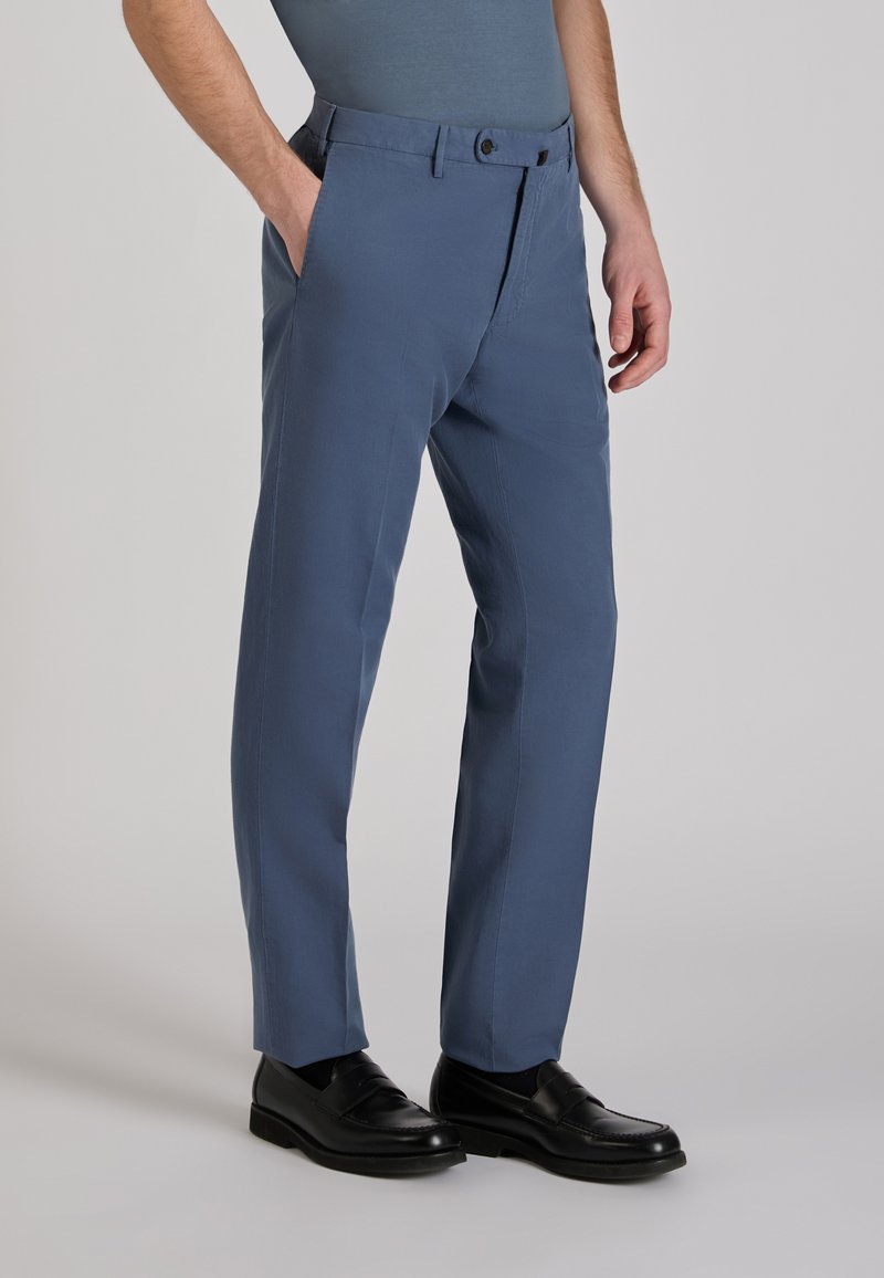 Blue trousers made of fabric with a smooth texture, featuring side pockets, a zip fly, and a button closure, paired with black shoes.