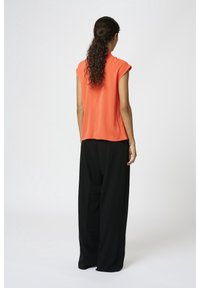 Haut orange à manches courtes avec une coupe décontractée, associé à un pantalon noir ample. Texture lisse et tissu léger.