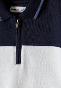 Polo pour enfants bleu marine et blanc texturé avec une fermeture éclair et une étiquette de marque indiquant "minoti" pour les enfants de 5 à 6 ans.