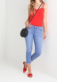 Top rojo de tirantes, jeans skinny azul claro, sandalias rojas tipo deslizamiento con detalle de lazo y un bolso cruzado negro circular.