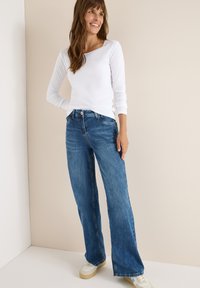 Hvid langærmet skjorte med firkantet halsudskæring, parret med blå vide jeans og hvide sneakers. Glat stof, afslappet pasform, casual stil.