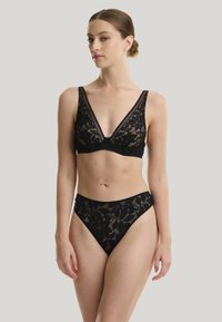 Schwarzer Spitzen-Bralette mit V-Ausschnitt und breiten Trägern, kombiniert mit passenden Spitzenunterhosen mit floralen Mustern und strukturierten Akzenten.