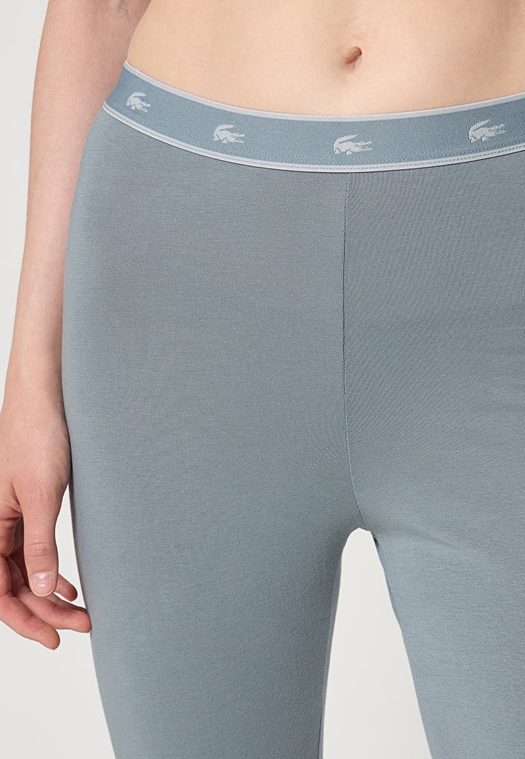Leggings grises fabricados con un tejido elástico, que cuentan con una cinturilla suave y un sutil patrón de logo. Textura suave y diseño ajustado.