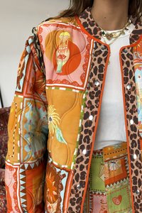 Gequilted jas met levendige oranje, roze en groene patronen, een luipaardprint rand, drukknoopsluiting en textuurstoffen met bloemmotieven.