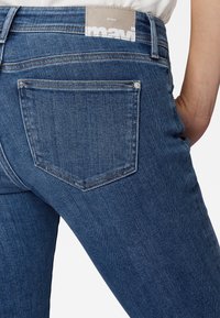 Jeans de mezclilla azul oscuro con un diseño ajustado, con un ligero desvanecimiento y detalles de costura, un bolsillo trasero y una etiqueta de cuero con marca en la cintura.