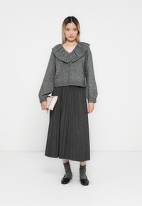 Sivý pletený cardigan so širokým rebrovaným golierom, skombinovaný s plisovanou sivou sukňou. Outfit dopĺňa svetloružová kabelka a sivé ponožky.