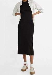 Abito nero midi dallo stile aderente, con scollo a giro, abbinato a una camicia a righe oversize e sneakers beige con dettagli rossi.