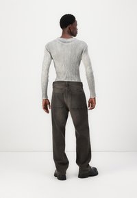Tettsittende ribbet grå langermet topp, kombinert med løse mørkegrå jeans med to baklommer og svarte kraftige sko.
