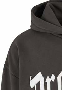 Mørk grå hettegenser med en myk tekstur, med et stort hvitt grafisk design på framsiden og en klassisk kengurulomme.