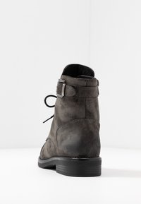 Bottine en daim gris avec bout rond, design à lacets, et une solide bride de cheville avec ferrure métallique. Surface texturée et semelle plate.