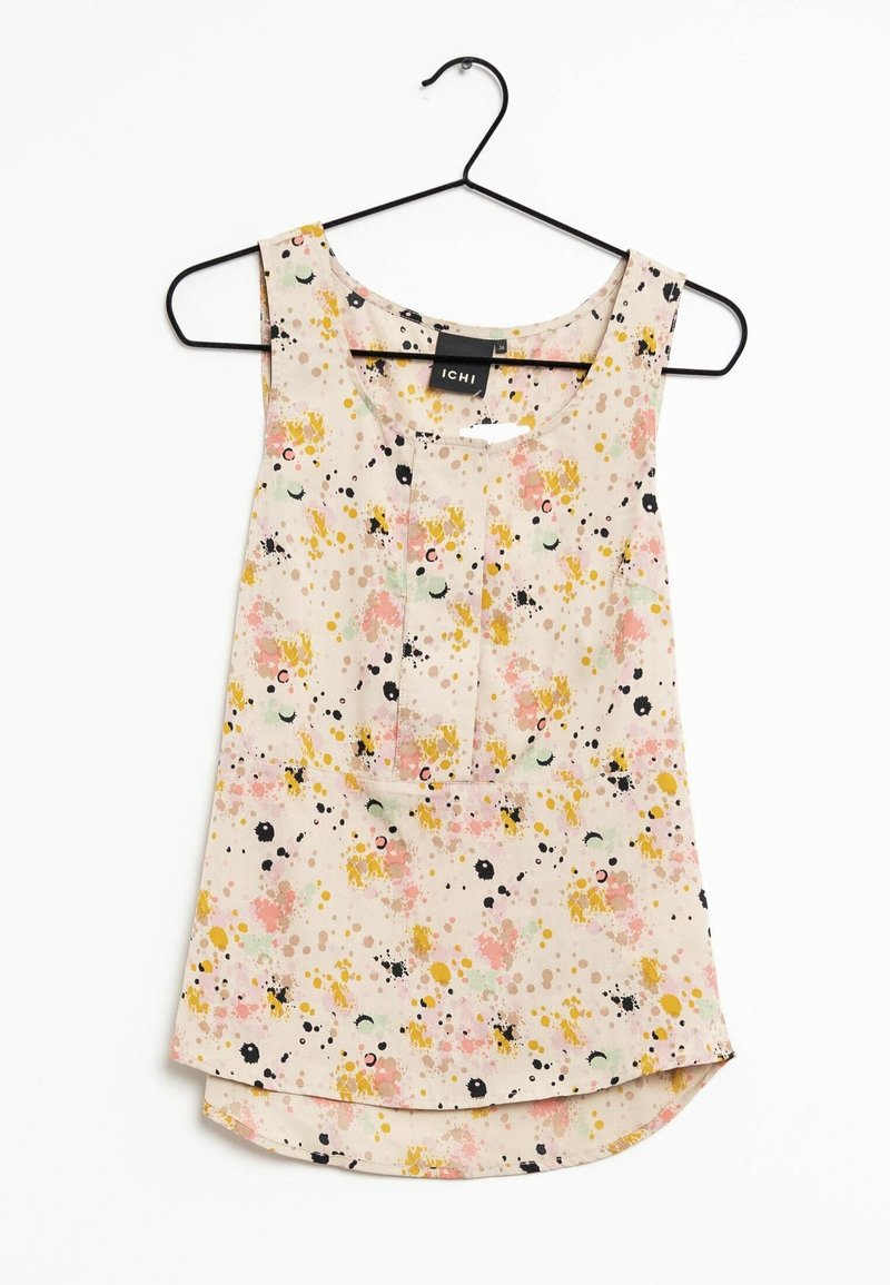 Blouse sans manches beige clair avec des motifs abstraits éclaboussés rose, jaune et noir, suspendue sur un cintre noir sur fond blanc.