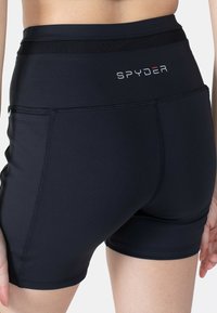 Černé sportovní šortky s vysokým páskem, vyrobené z elastického materiálu, s viditelným šitím a logem na zadní straně. Dvě boční kapsy.
