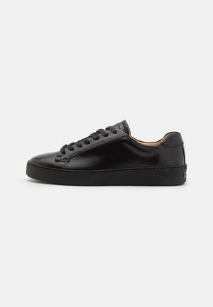 Czarny, niski skórzany sneaker z czarnymi sznurowadłami i grubą gumową podeszwą, przedstawiony z boku na jednolitym białym tle.