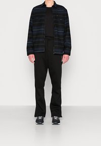 Czarna i niebieska kurtka w paski z dwoma kieszeniami na piersi, zestawiona z czarnymi spodniami i sportowymi butami. Gładki materiał i luźny krój na całej długości.