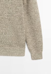 Beige and brown marled knit sweater sleeve with ribbed cuffs and hem on a white background.