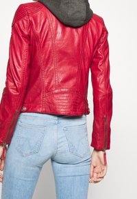 Giacca di pelle rossa con design aderente, caratterizzata da spalle trapuntate e polsini con zip, abbinata a jeans azzurri chiari.