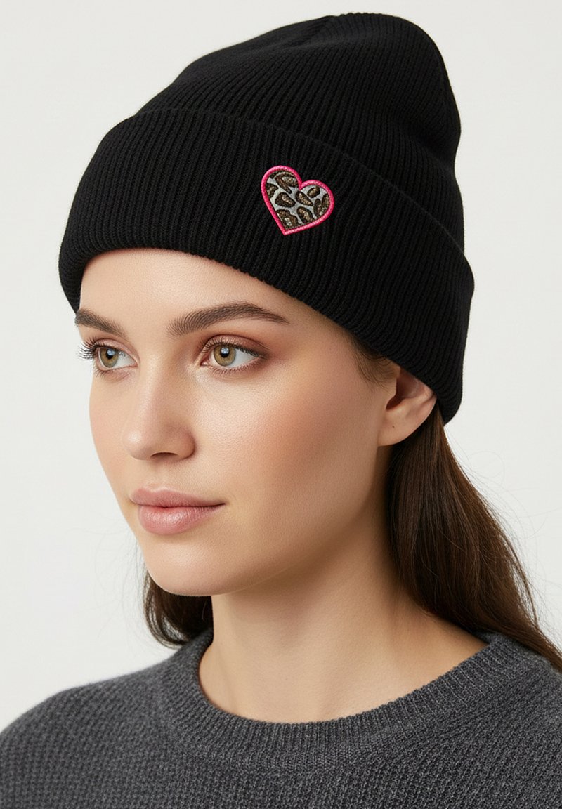 Black ribbed knit beanie with a pink outlined heart patch featuring a leopard print design. Soft texture and snug fit highlighted.