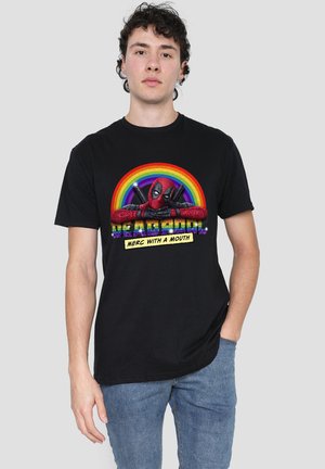 Young man wearing black Deadpool t-shirt with rainbow and "Merc with a Mouth" text, standing against plain light gray background.
