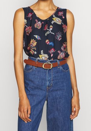 Ärmelloses marineblaues Oberteil mit buntem Blumenmuster, kombiniert mit hoch taillierten blauen Jeans und einem braunen Gürtel mit goldener Schnalle.