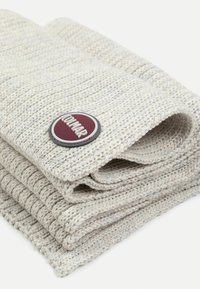 Foldet strikket tæppe i lys grå, med et tekstureret mønster. Inkluderer et rundt logo-patch i burgunder og sølv.