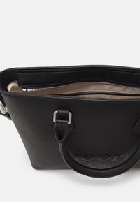 Črna usnjena torbica z teksturirano zunanjostjo, zgornjim zadrgo in bež notranjostjo. Ima kratke črne ročaje in vtisnjen logotip.