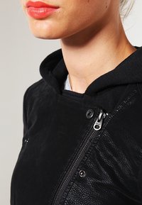 Felpa nera con finitura testurizzata, dettagli con zip e bottoni a pressione. Tessuto morbido, presenta uno strato interno grigio a contrasto.