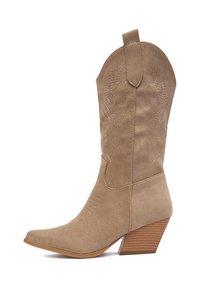 Beżowy zamszowy kowbojski but z zaostrzonym noskiem, skośnym drewnianym obcasem i wytłaczanymi kwiatowymi wzorami na cholewce. Posiada pętelkę ułatwiającą zakładanie.