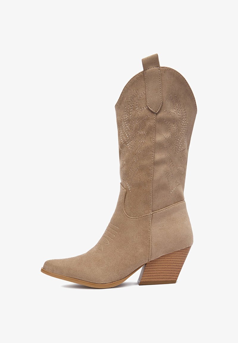 Beżowy zamszowy kowbojski but z zaostrzonym noskiem, skośnym drewnianym obcasem i wytłaczanymi kwiatowymi wzorami na cholewce. Posiada pętelkę ułatwiającą zakładanie.