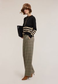 Maglione lavorato a maglia a righe nere e crema, pantaloni a vita alta a quadri verdi e beige, stivaletti con tacco color cuoio, cappello maculato, borsa nera.