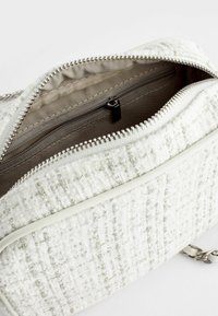 Witte handtas met textuur en ritssluiting. Interieur heeft een grijze voering en een klein ritsvakje. Ontworpen met metallic accenten en een kettingband.
