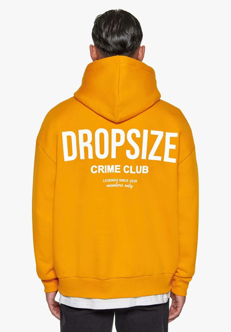Gul hættejakke med stor hvid tekst "DROPSIZE" over "CRIME CLUB" og mindre tekst nedenfor. Har en kengurulomme og justerbar hætte.