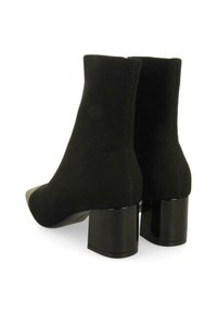 Botas de tobillo de punto negro con puntera redondeada y parte delantera beige en contraste, montadas sobre tacones de bloque brillantes. Tejido texturizado con cuello acanalado.