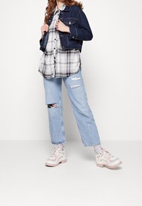 Giacca di jeans, camicia a quadri bianco e nero, jeans chiari strappati e sneaker chunky bianche-rosa con suole testurizzate. Look casual a strati.