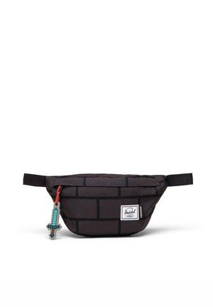 Banane noire avec motif de briques, porte-clés épée pixelisée, fermeture zippée sur le devant et écusson du logo Herschel sur fond blanc.