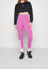 Czarny krótki top z długim rękawem i różowe legginsy o wysokim stanie z białymi bocznymi paskami. Czarne sportowe sneakersy dopełniają outfit.