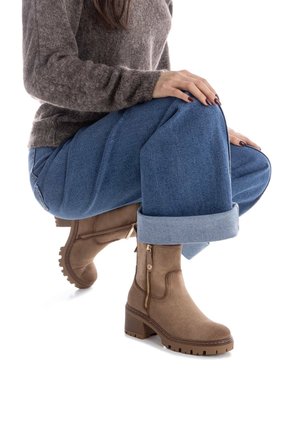 Stivaletti in suede marrone con zip laterale, tacco a blocco e suola texturizzata, abbinati a pantaloni blu con risvolto e un maglione grigio.