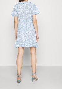 Ljusblå blommig klänning med korta ärmar, volangkant och figursydd midja. Matchas med ljusblå sandaletter med remmar. Inga framträdande mönster.