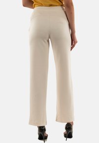Pantalones de pierna ancha color beige claro con una textura suave, cintura elástica y sin patrones visibles, combinados con tacones negros.