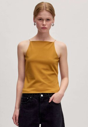 Mosterdgele mouwloze top met een vierkante halslijn, gemaakt van zachte stof, gecombineerd met hoge zwarte jeans. Eenvoudig, aansluitend ontwerp.